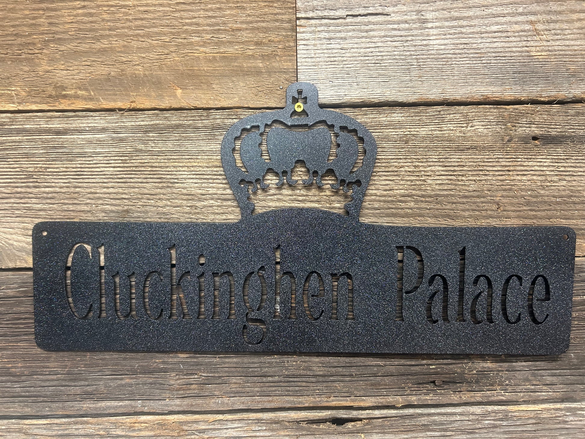Decorative metal sign with 'Cluckington Palace' text and crown design on a wooden background