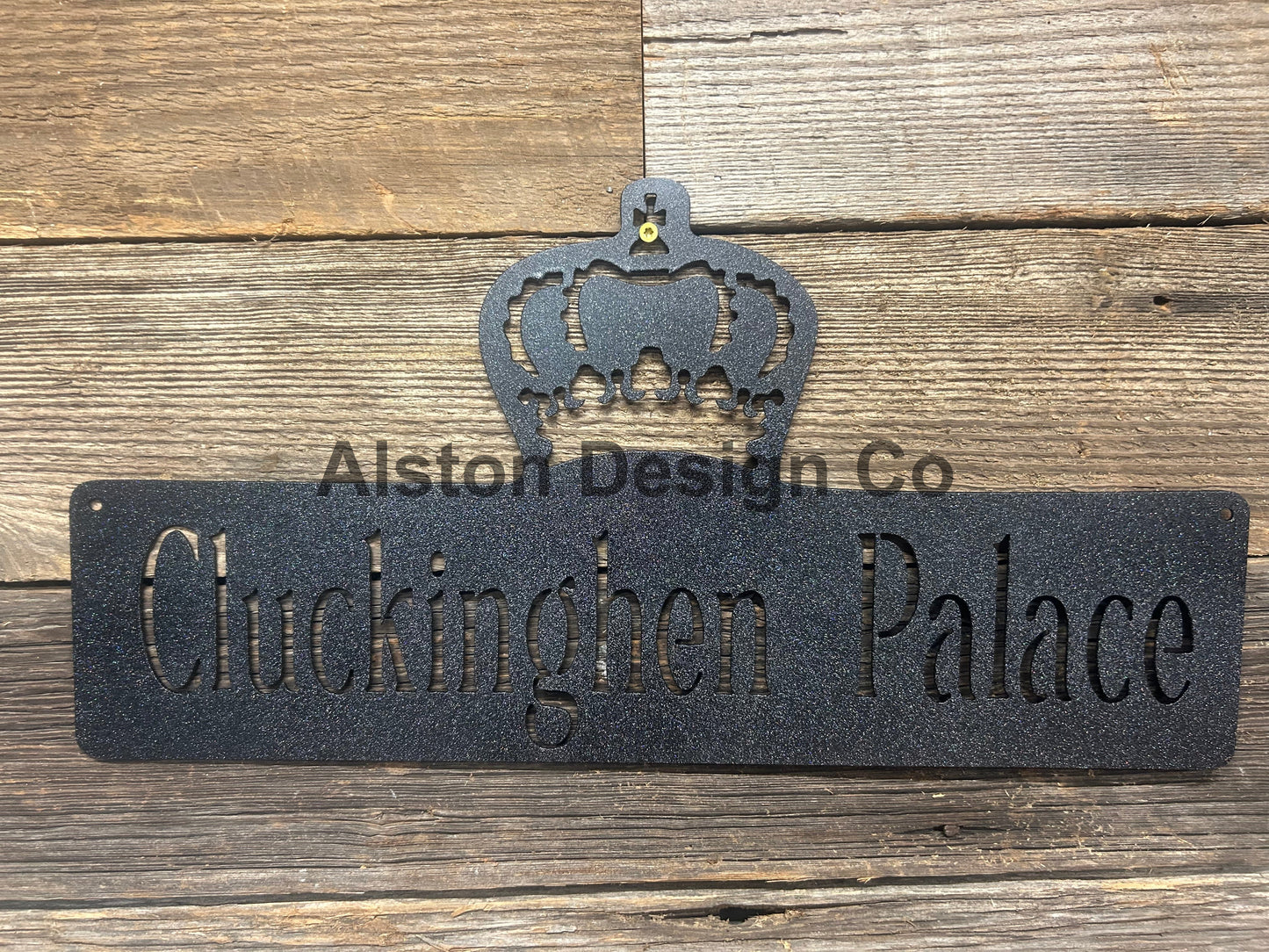 Decorative metal sign with 'Cluckington Palace' text and crown design on a wooden background