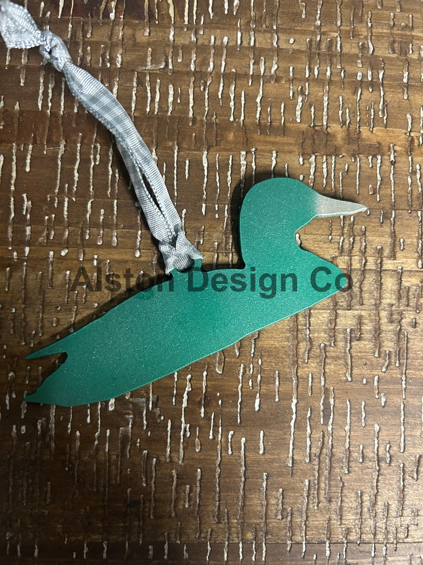 Green metal duck with a ribbon on a wooden surface