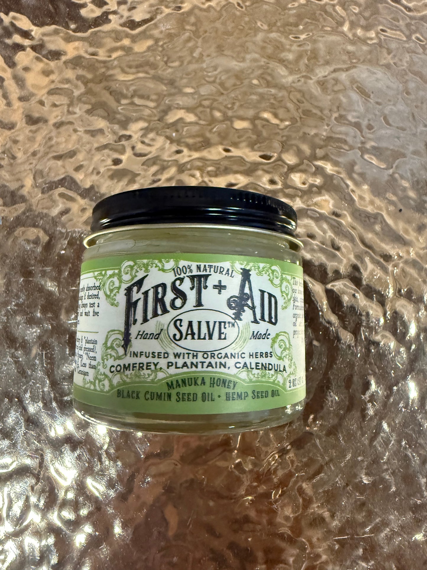 Jar of First Aid Salve with green label on a textured surface