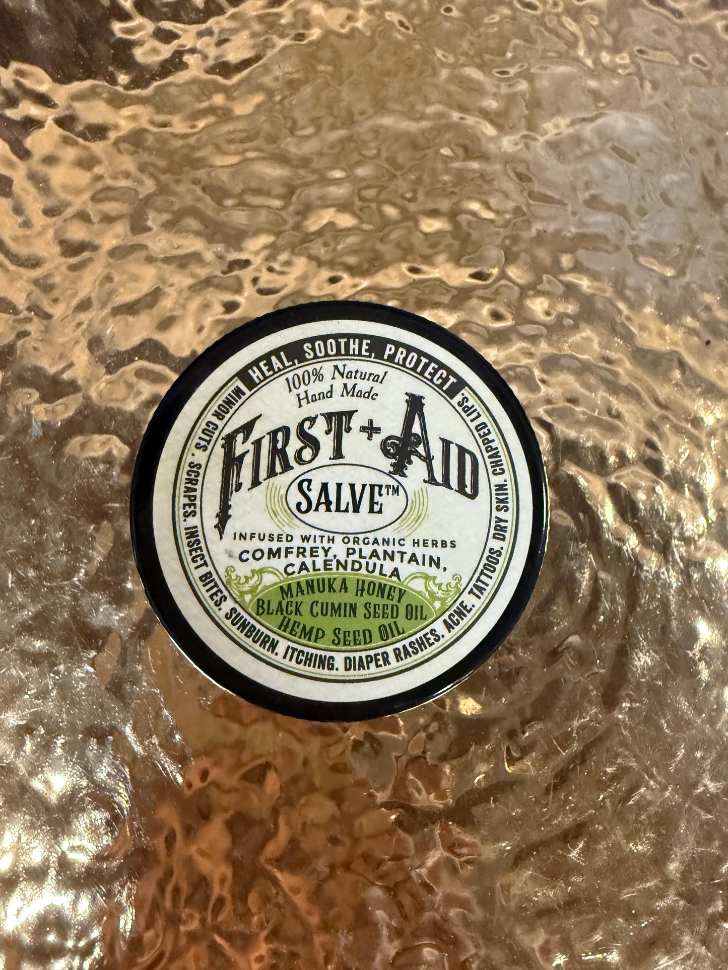 Round container of First Aid Salve on a textured surface